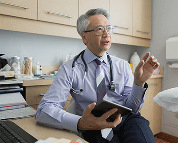 Asian doctor facing right speaking with tablet in hand.