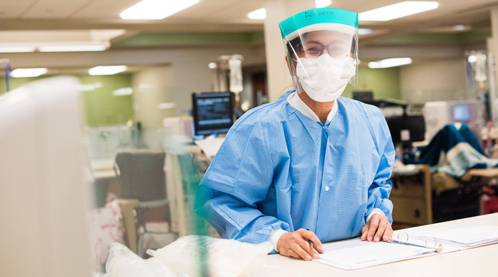 Clinical worker in personal protective gear standing at a desk reviewing paperwork